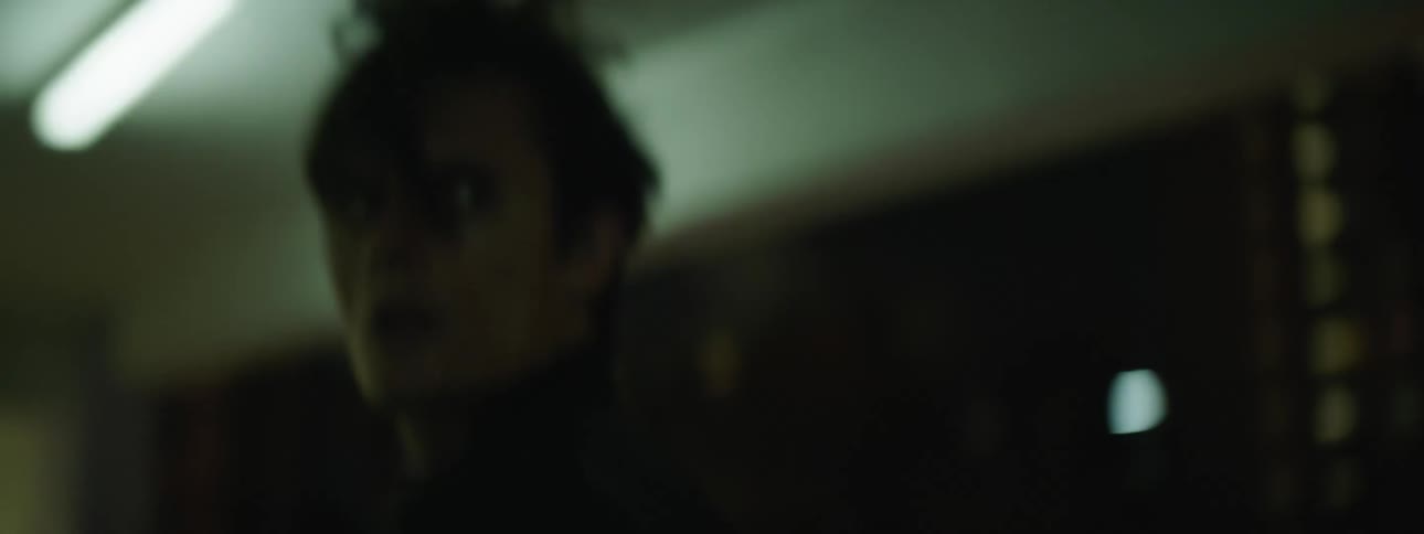 A man in a black leather jacket running down a hallway while checking behind himself