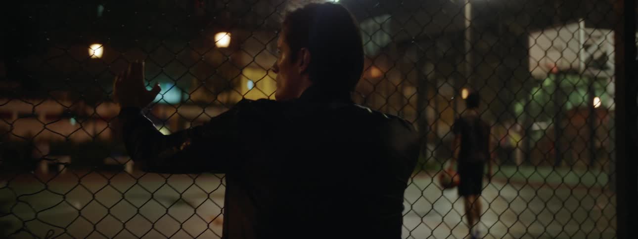 A man looking through a fence of a basketball court
