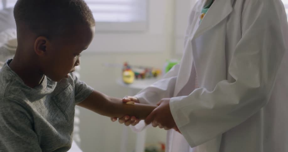A doctor smooths a bandage on a black boys arm