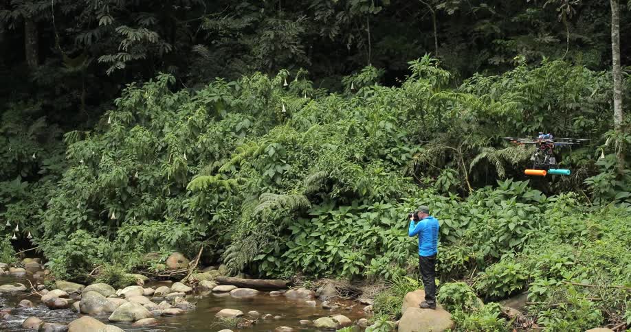 A man takes photographs while a drone hovers behind him
