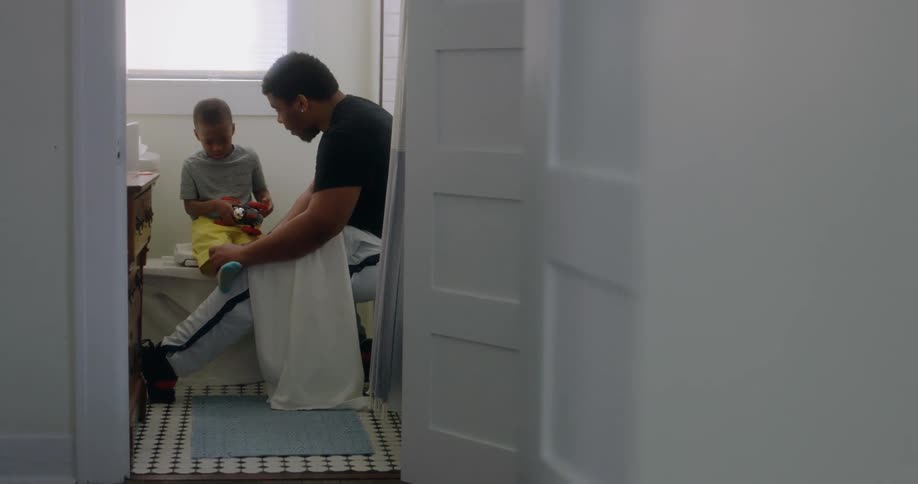 A man sits in the bathroom and puts a bandage on his toddler son