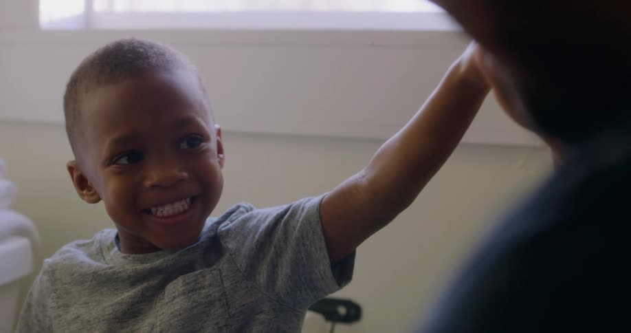 Son sitting on toilet in the bathroom smiles and his father holds up his hand and gives him a high five