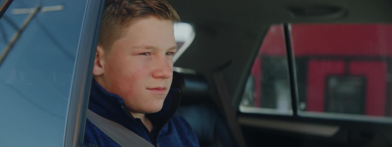 A boy sitting in the backseat of a car with the seatbelts on