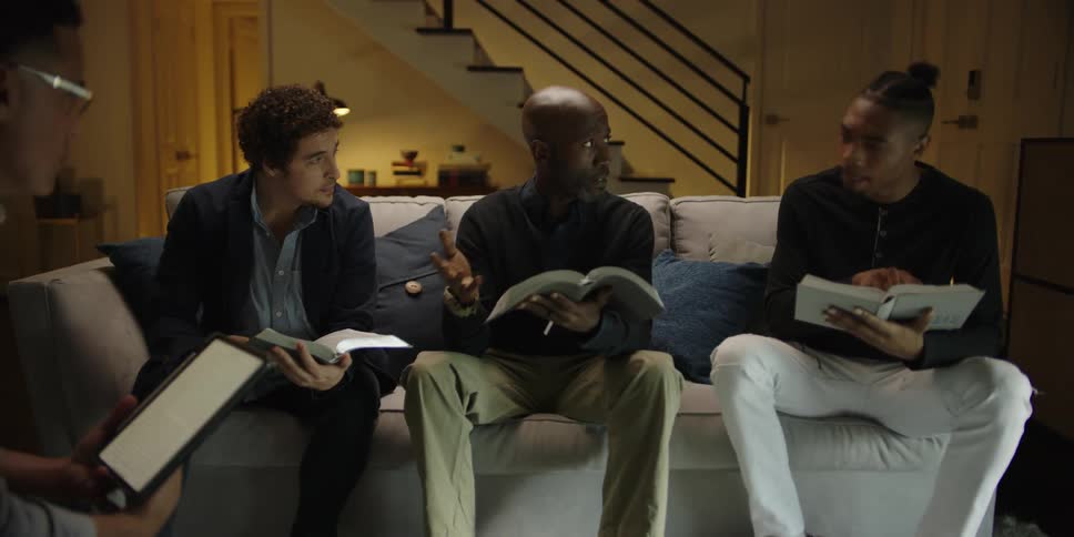 A group of men sit around a room having a bible meeting