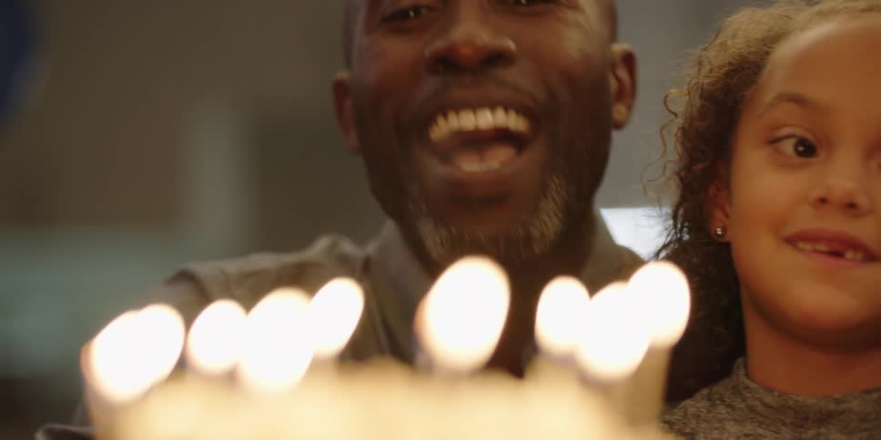Father holding daughter blows out candles on birthday cake
