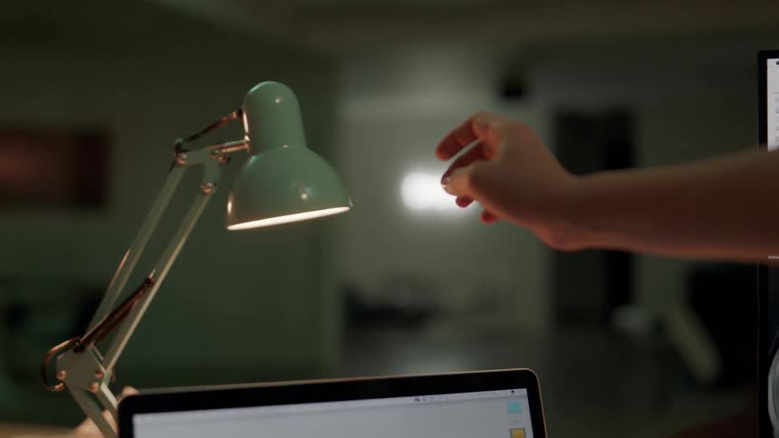 Person reaches toward flickering desk lamp near computer display