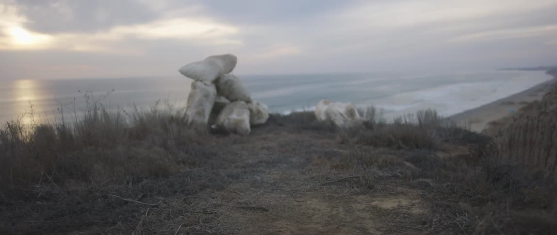 Sandbags sit in a pile at the top of a cliff overlooking the ocean
