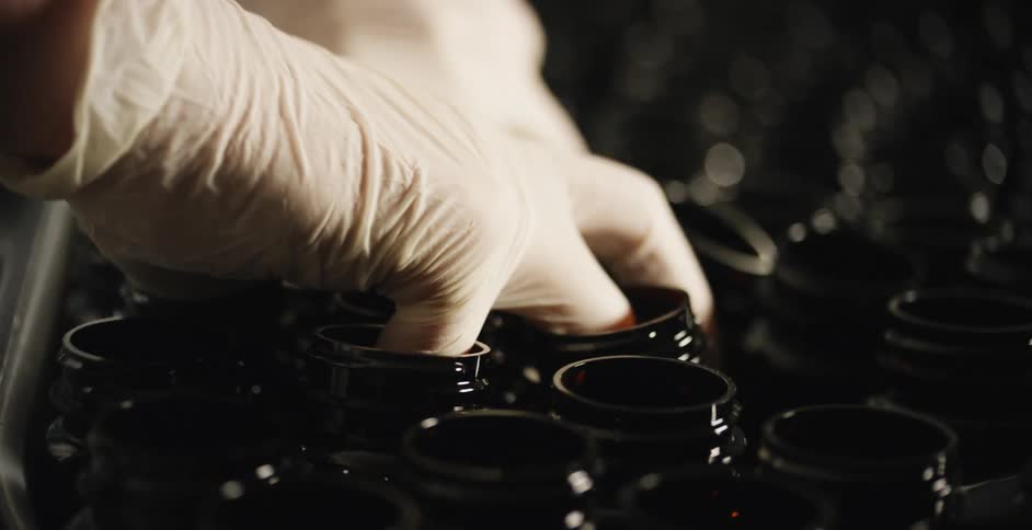Hands wearing white gloves pick up bottles by inserting fingers and moving them