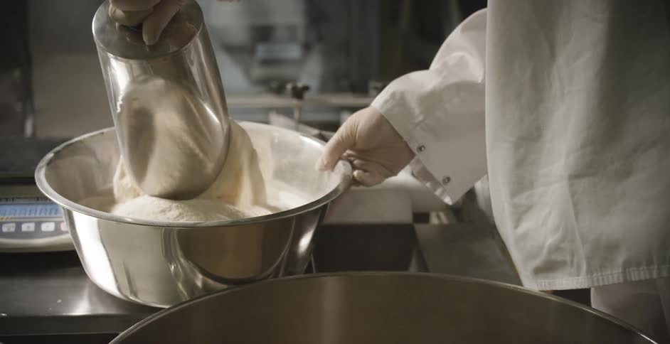 Pastry chef pouring flour from scoop into large metal bowl