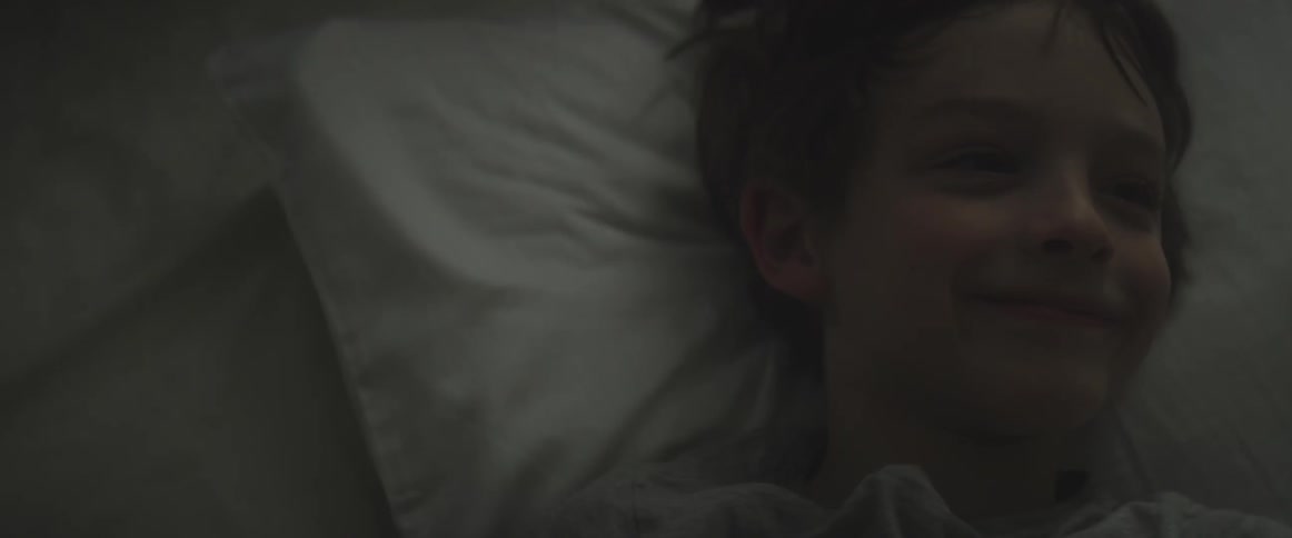 A boy lays smiling in bed