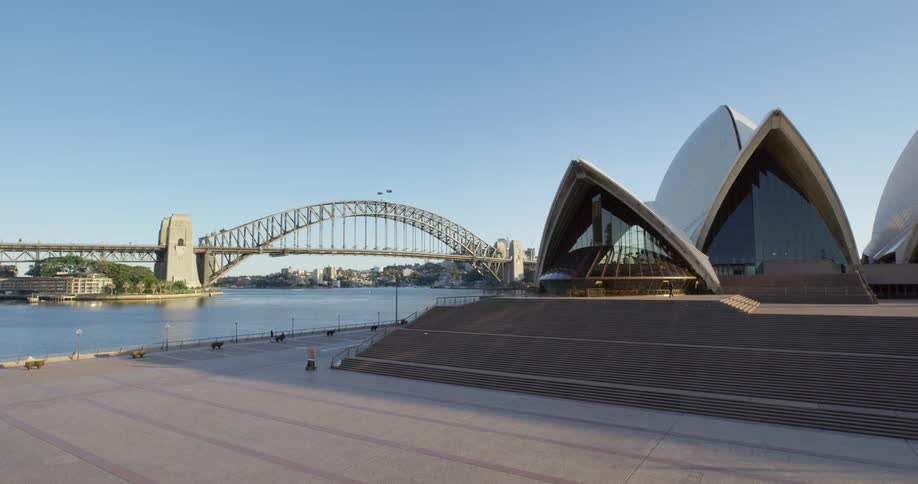 Person walks near sydney opera house under a clear blue sky