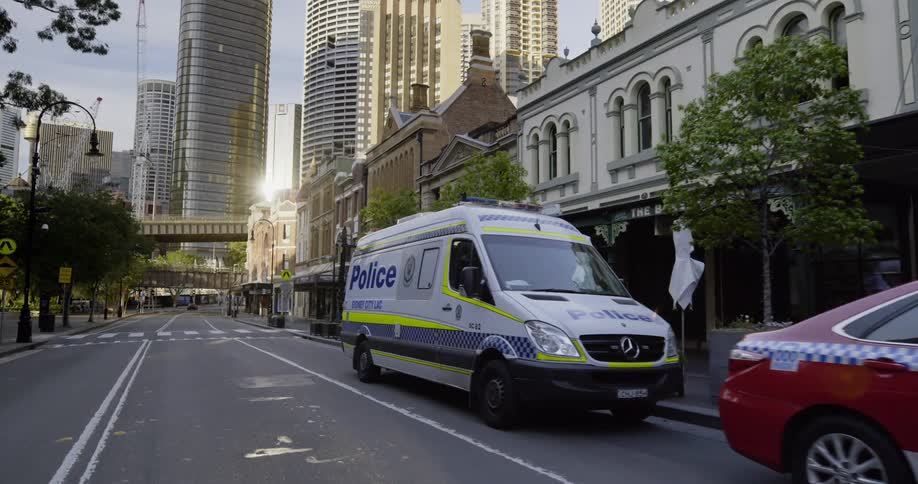 Three police vehicles sit on the side of the road in a large city