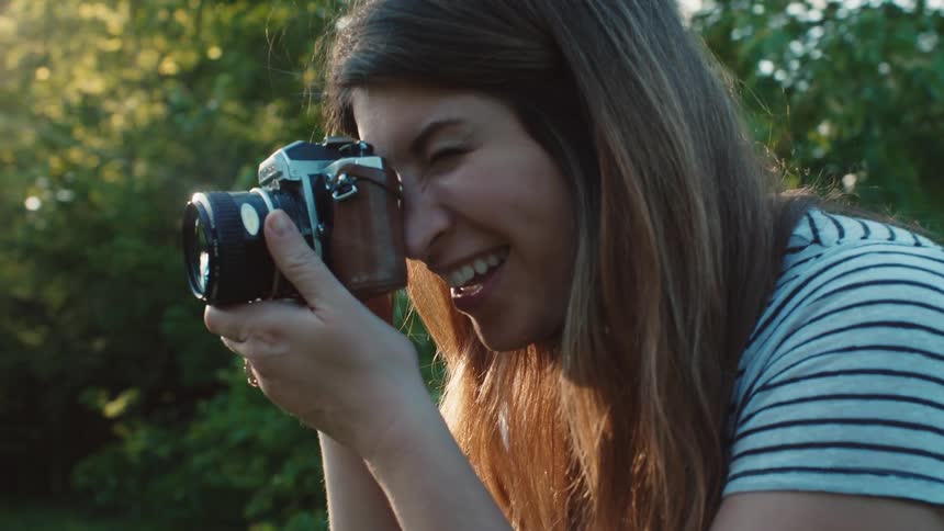 A woman in an outside yard holds a camera up to her face