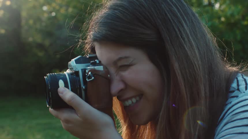 A white woman takes a picture with a camera and smiles