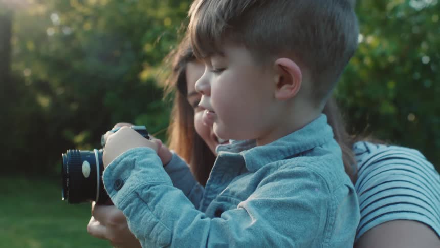 A mother and toddler son look at a camera in a back yard setting