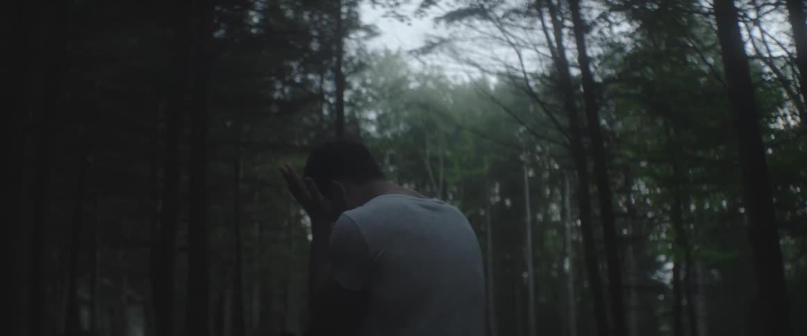 Man standing in a forest with his face in his hands