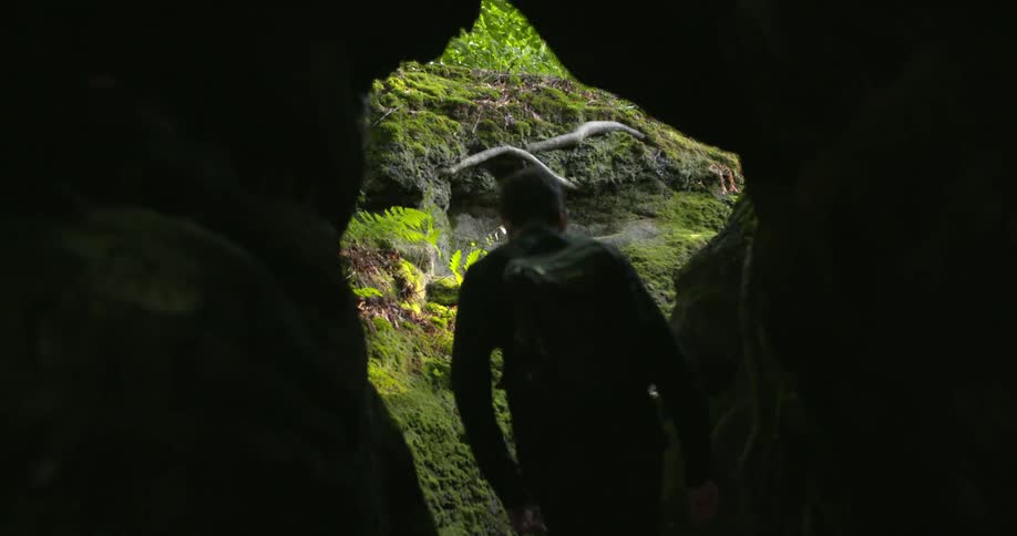 A hiker walks out of a cave into a forest