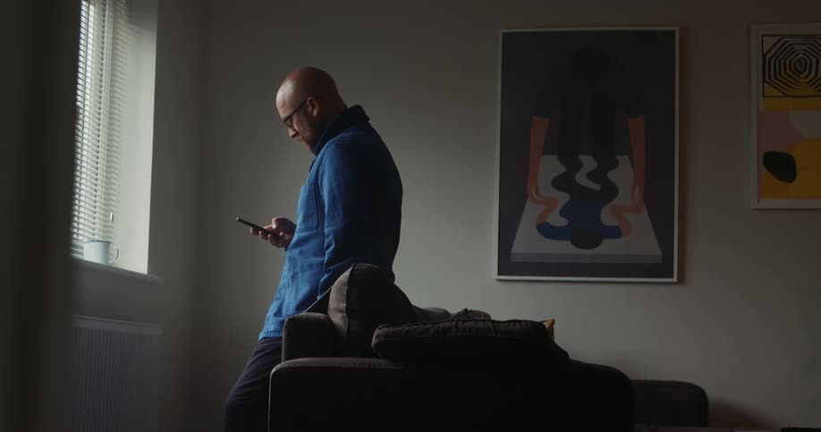 Man scroll through mobile phone leaning against couch