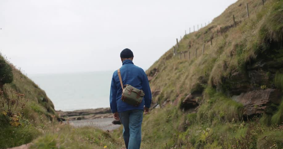 A man carefully walks across a rocky terrain by the ocean coast