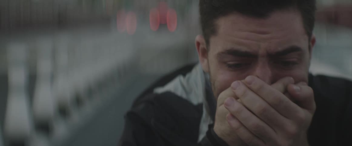 A man is standing outside crying with his hands clasped tightly over his mouth