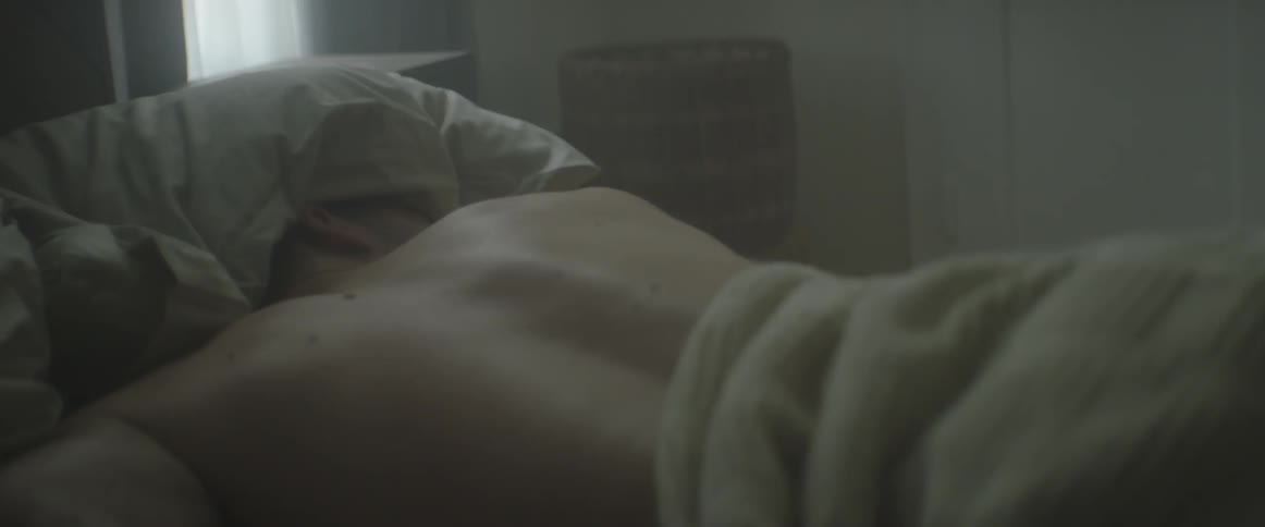 A man lies in bed on his stomach with a pillow over his head