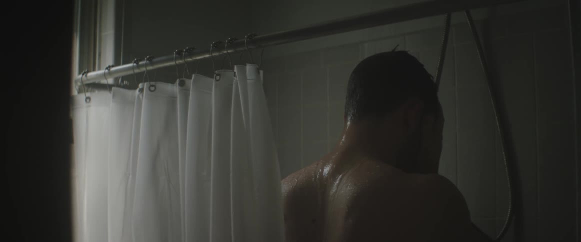 A man standing in the shower running his hands over his head