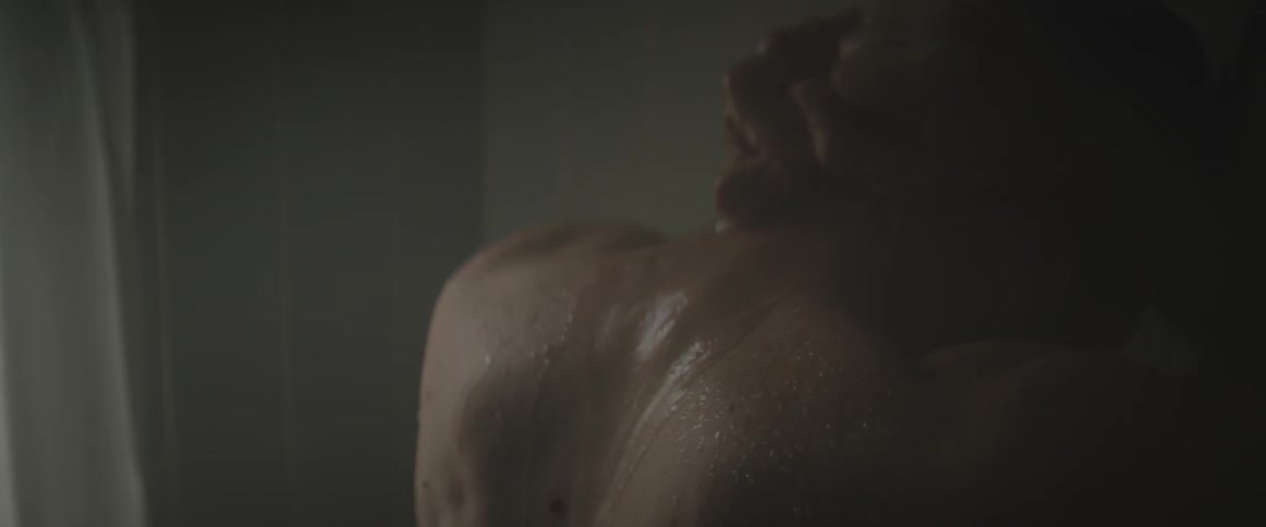 A man balls his fists tightly behind his neck as he showers