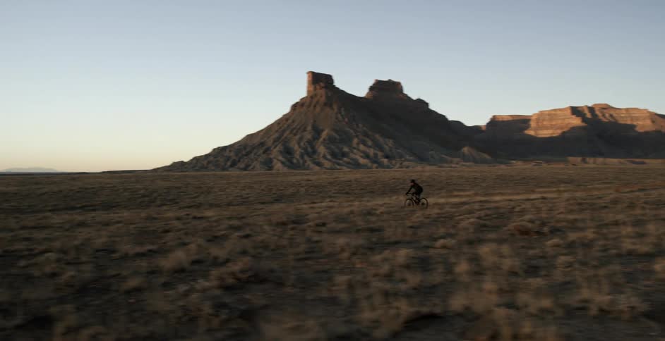 A person cycles across the desert countryside
