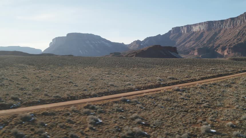 A person cycles down a dirt road towards canyons