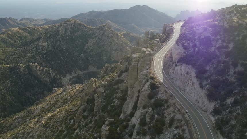 A narrow two lane road curves through the mountains as a cyclist climbs