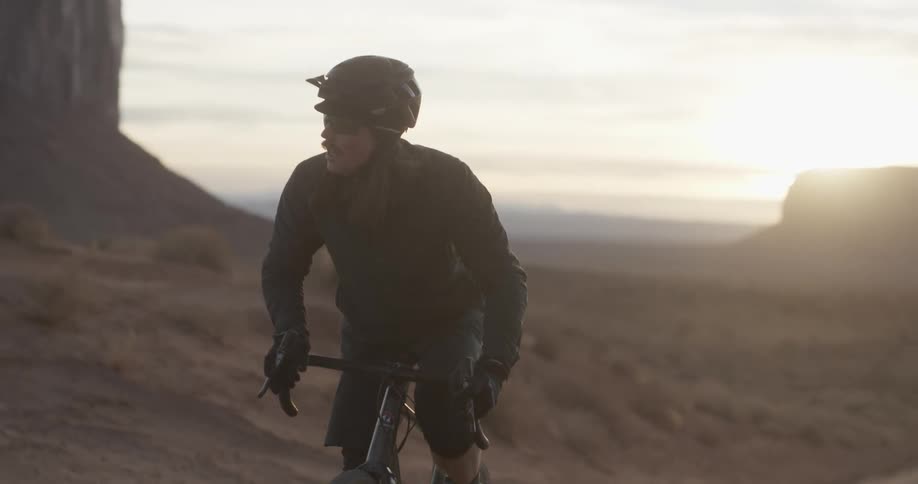A male bicyclist rides through a desert at sunrise