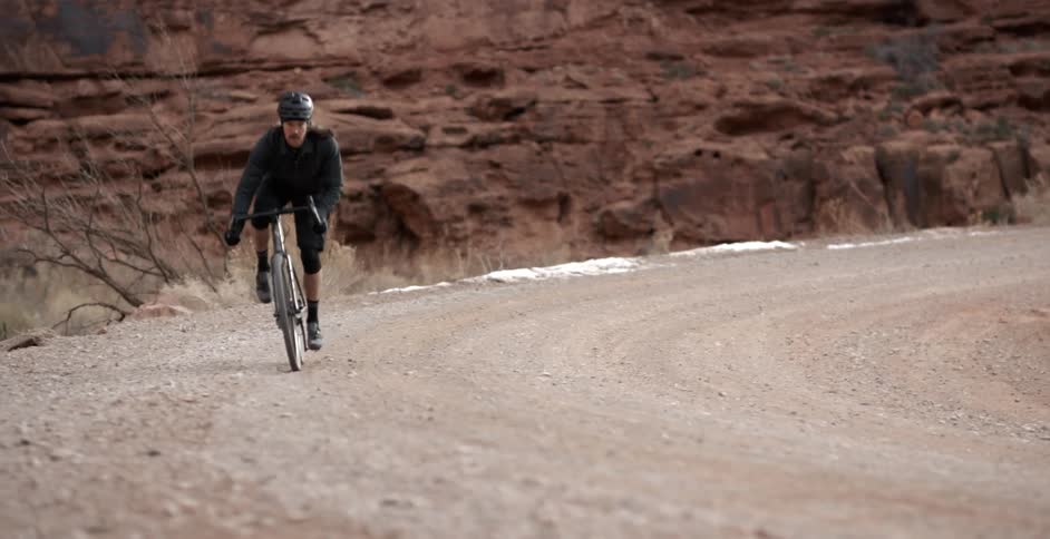 A cyclist stands as he pedals up a curve with red rock behind him
