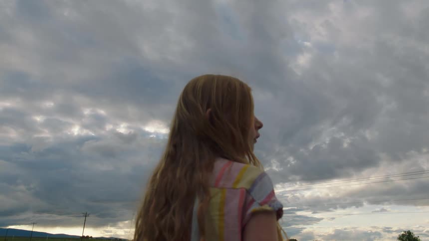 Little child looks around in the field on a cloudy day
