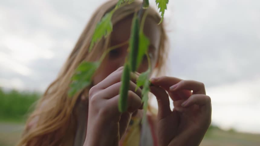 A woman is outdoors and looking at a leaf from a plant