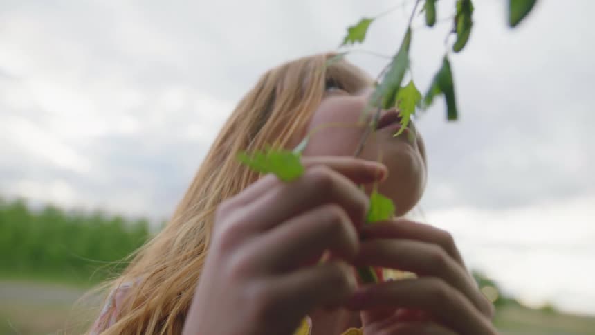 Little girl fiddles with a branch of a tree on a cloudy day