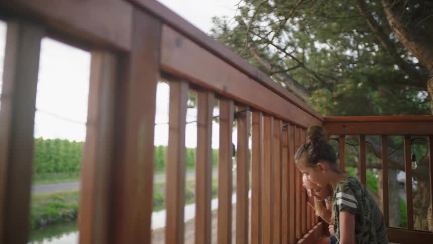 Two girls sit on a deck and look down and laugh