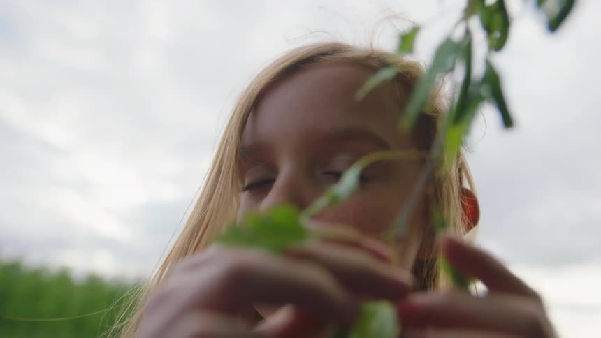 Blonde little girl plays with a branch of a tree