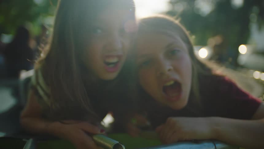 A pair of girls lying atop a trampoline while making funny faces at the camera