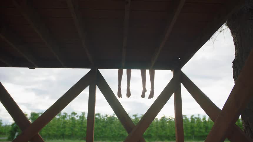 Two friends sitting side by side on a wooden deck swing their bare feet hanging over the edge