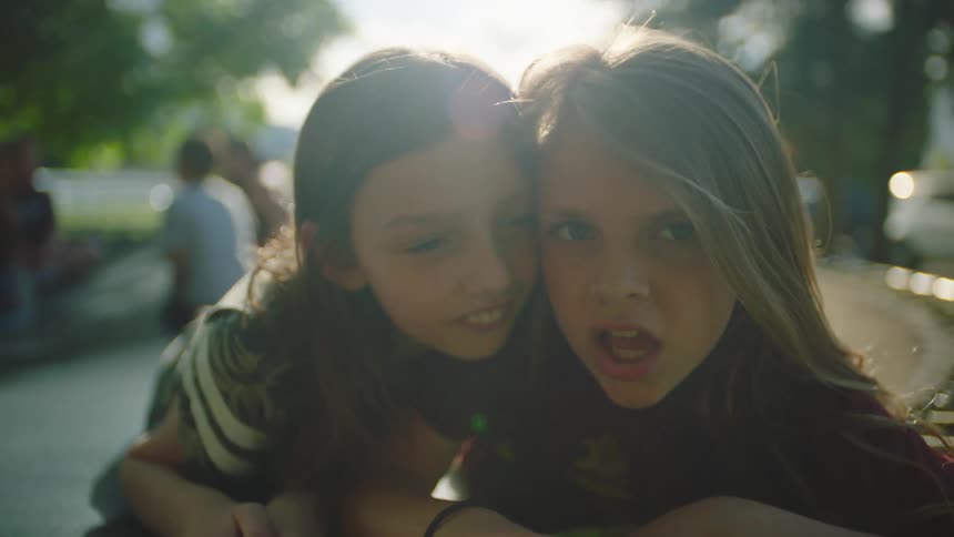 Two girls on a trampoline with other children the sky and trees in the background
