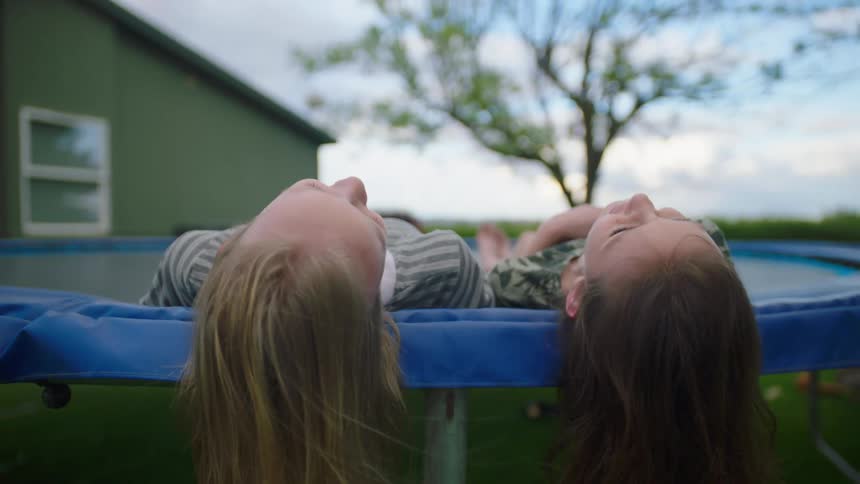 Two young white girls recline on a trampoline outside a house