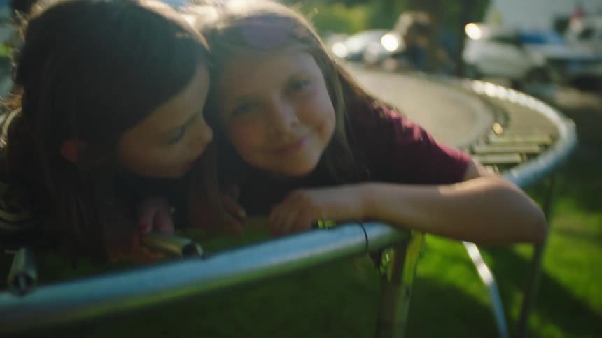 Two girls lie on trampolines laughing and hamming it up near others