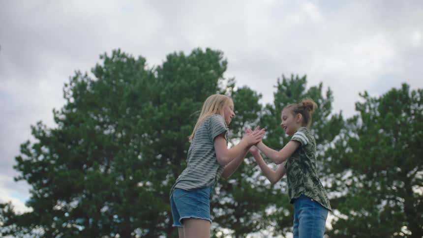 A pair of girls playing a clapping game while jumping on a trampoline
