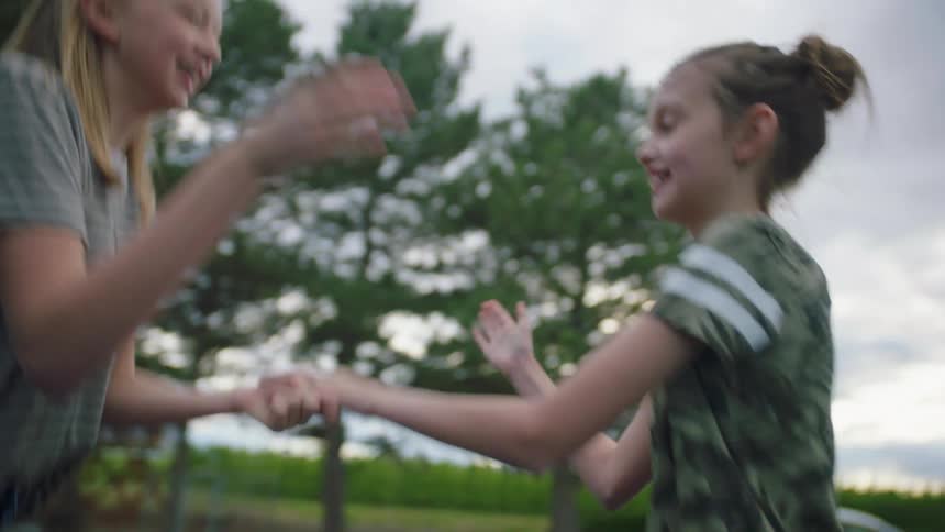Two girls playing clapping games while jumping together on a trampoline