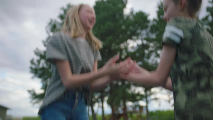 Two girls try to clap their hands together as they laugh and jump on a trampoline