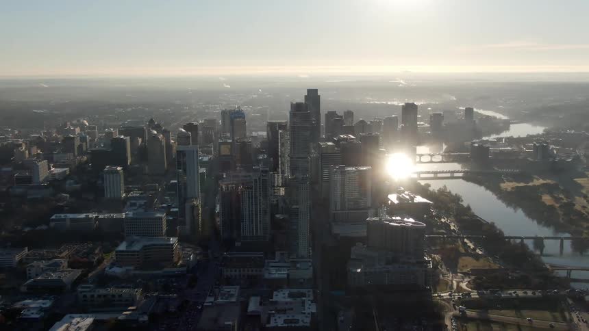 Vehicles cross a bridge over the river and head toward downtown as the sun rises