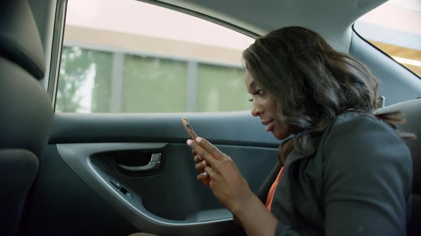 Woman sits in rear seat of moving car scrolling on mobile phone
