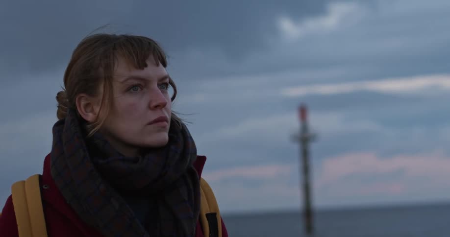 A woman stands outside wearing a large black scarf and carrying a yellow backpack