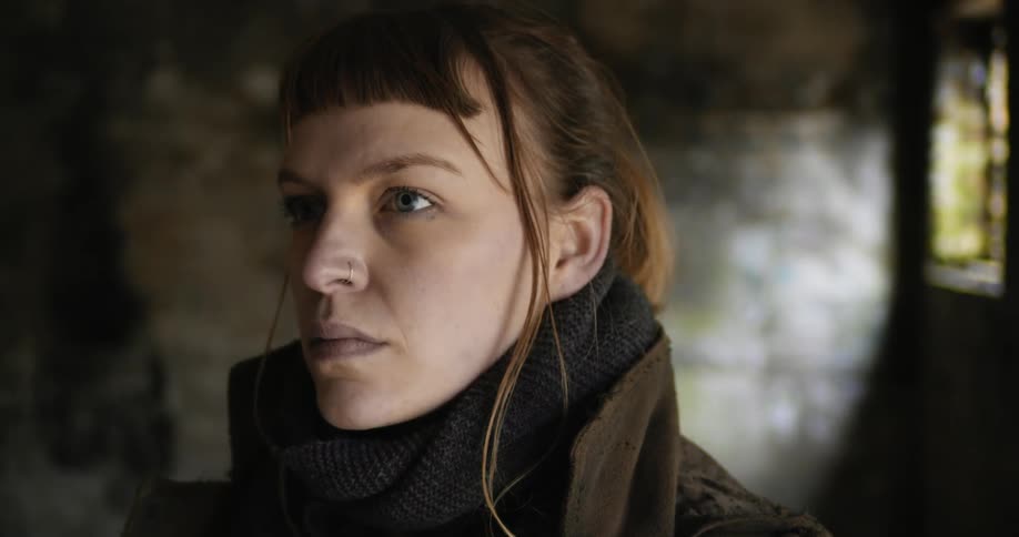 A white woman stands inside a room and looks off into the distance