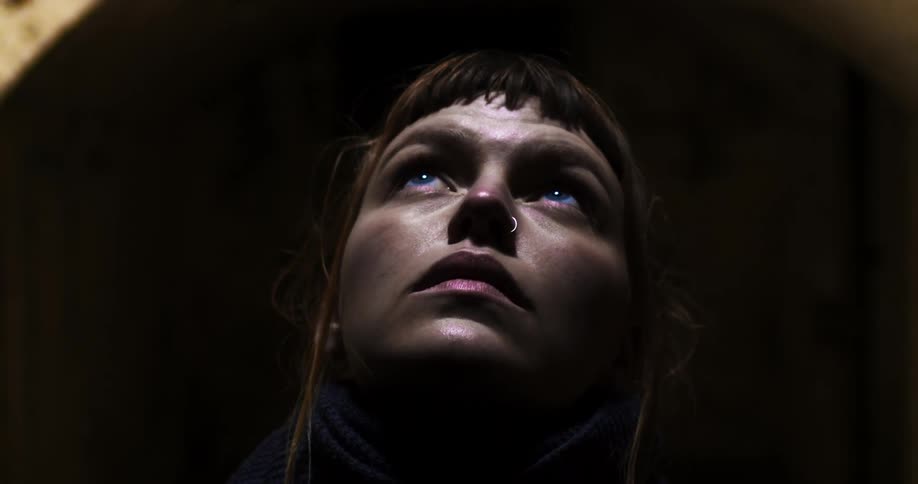 A dark haired woman looks up from a dark place